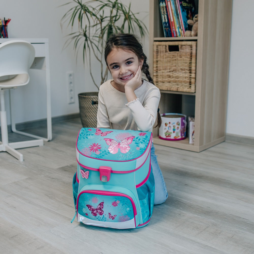 Mädchen sitzt im Wohnzimmer mit Händen auf Schulranzen gestützt und lächelt