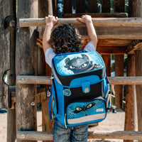 Junge mit Locken trägt den Dragons Schulranzen beim Klettern auf dem Spielplatz