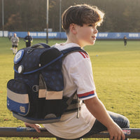 Junge trägt den HSV Ranzen am Sportplatz und schaut in die Ferne