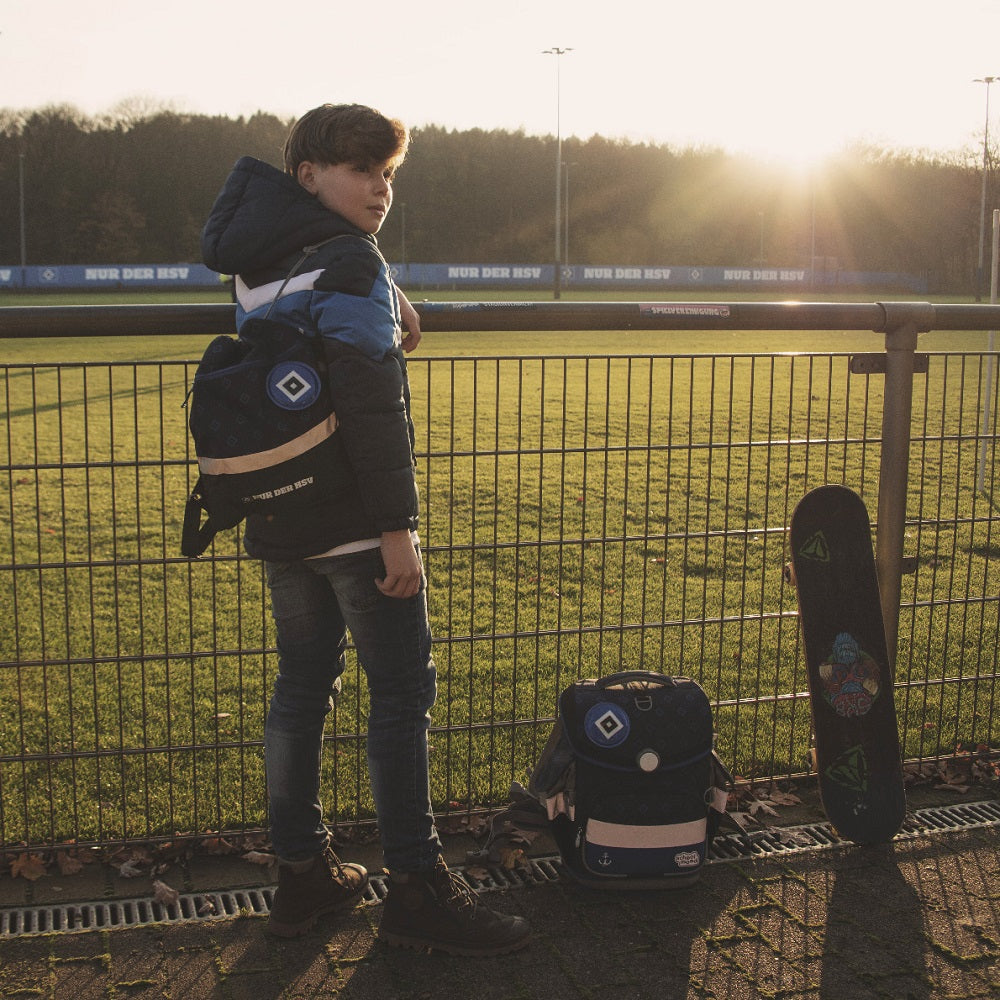 Junge trägt den zum Ranzen passenden Turnbeutel lässig am Sportplatz